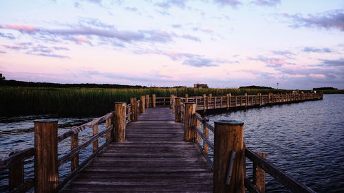 Wooden pier on jetty leading towards sea against sky