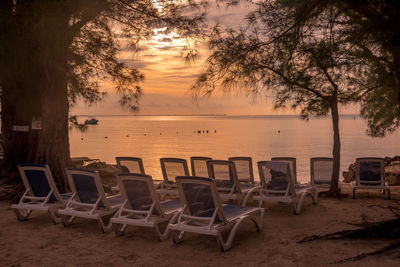 Empty chairs on beach against sky during sunset