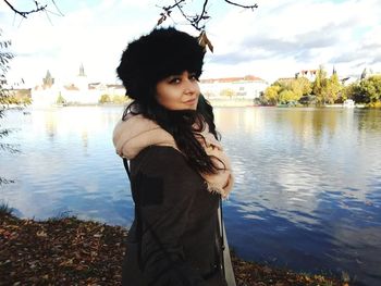 Portrait of young woman standing by river against sky