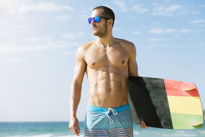 Full length of shirtless man standing by sea against sky