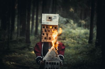 Man holding burning model house while standing on field in forest
