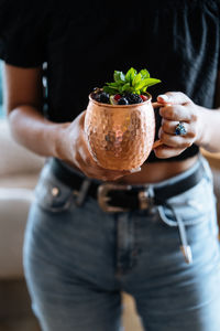 Unrecognizable female carrying metal mug of natural fruit drink with berries and mint leaves on summer day in cafe