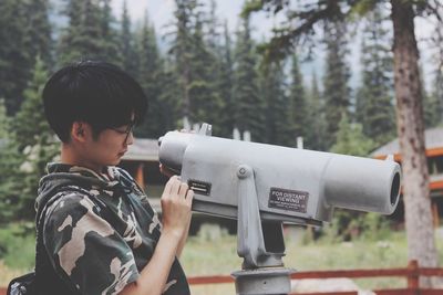 Side view of man looking through binoculars in forest