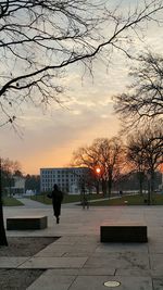 Man walking by bare trees against sky during sunset