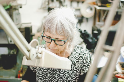 Senior woman wearing glasses while working in jewelry workshop