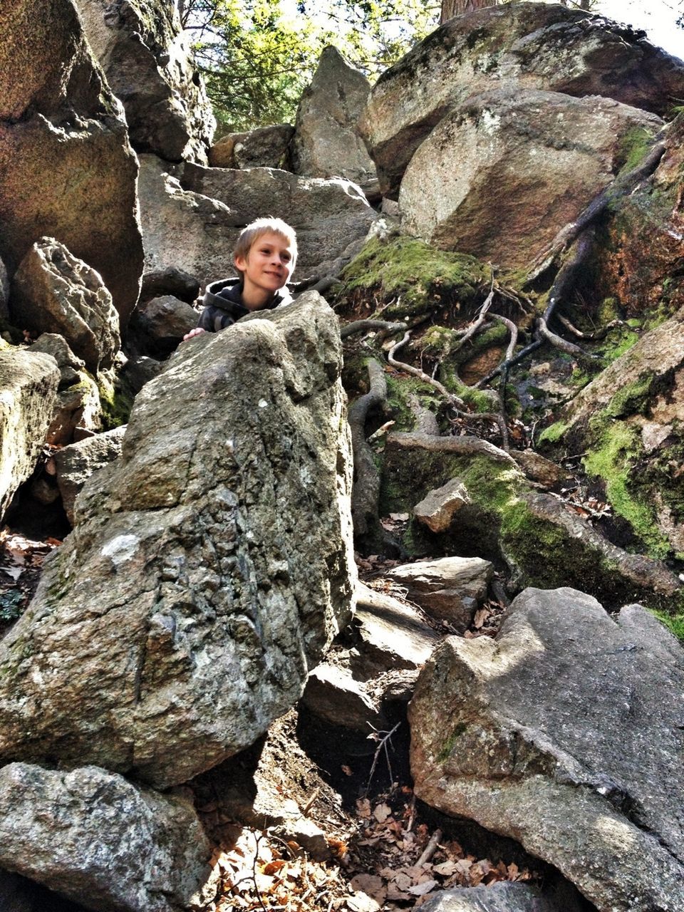 rock - object, rock formation, young adult, rock, lifestyles, full length, leisure activity, textured, person, nature, standing, low angle view, tree, casual clothing, day, cliff, outdoors, stone wall