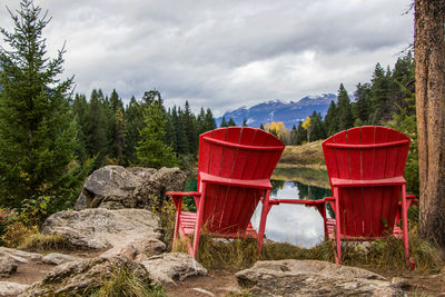 Red chairs on rocks by trees and a lake against sky in jasper national park 