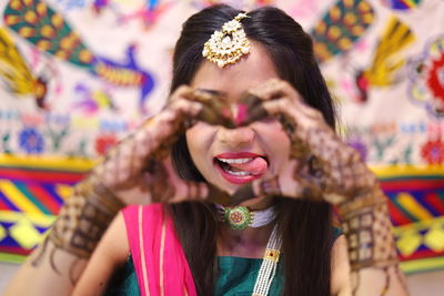 Woman making heart shape and sticking out tongue during haldi ceremony