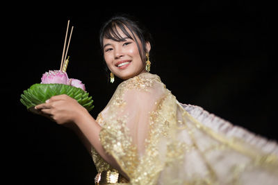 Portrait of young woman wearing wedding dress standing against black background