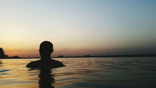 Silhouette man swimming in lake against sky