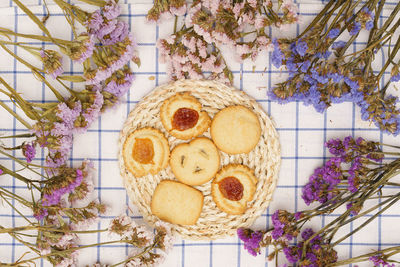 Flat lay of sweets, butter cookie on rattan plate in center of statice flower on blue gingham cloth.