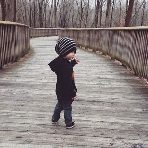 Full length of boy standing on boardwalk in forest