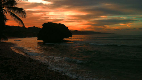 Silhouette view of rocks in sea against dramatic sky