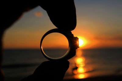 Close-up of silhouette hand against sea during sunset