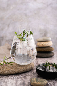 Gin tonic with ice and rosemary in a glass on a stone on the table vertical view