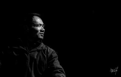 Portrait of young man looking away against black background