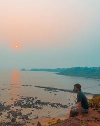 Man looking at sea against sky during sunset