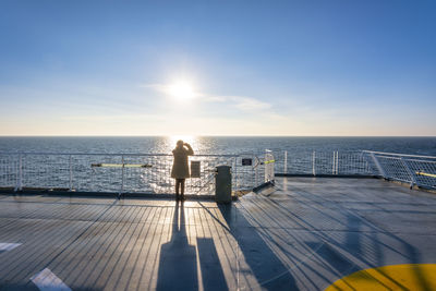 Uk, scotland, lone woman looking at setting sun from afterdeck of moving ferry