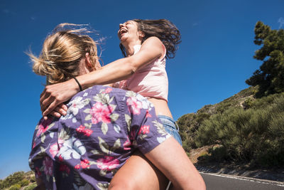 Boyfriend carrying cheerful girlfriend on road during sunny day