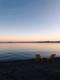 Chair on beach against sky during sunset