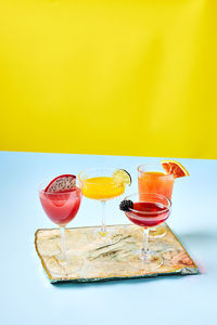 4 tropically colored cocktails on blue and yellow background