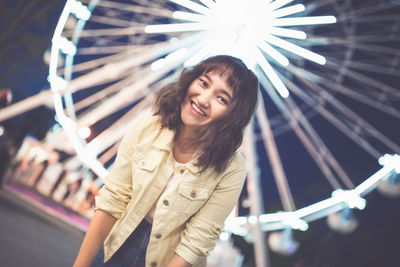 Beautiful asian girl in an amusement park at nght, smiling. ferris wheel in the background