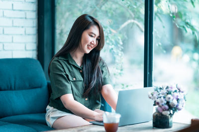 Portrait of young woman using mobile phone while sitting at home