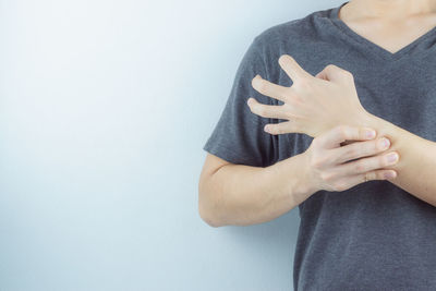 Midsection of woman holding hands against white wall