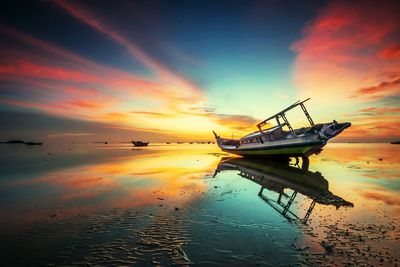 Fishing boat moored in sea against sky during sunset