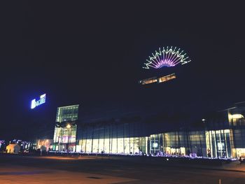 Illuminated ferris wheel by buildings in city at night