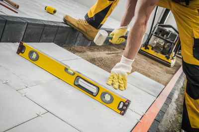 Caucasian construction worker with professional hammer in his hand building concrete tiles pathway.