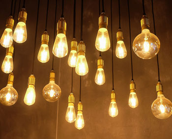 Low angle view of illuminated light bulbs hanging against wall in room