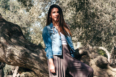 Portrait of smiling young woman standing against tree trunk