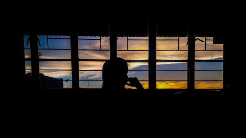 Rear view of silhouette man sitting in glass window