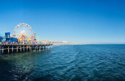 Ferris wheel by sea against clear blue sky