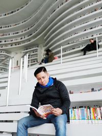 Young man reading book while sitting in library