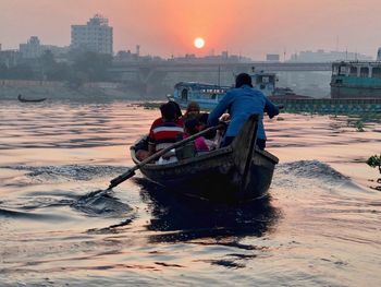 Rear view of people in sea against sky during sunset