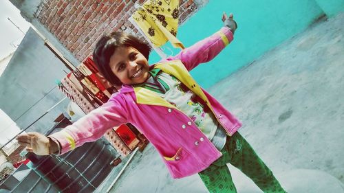 Portrait of cheerful girl with arms outstretched standing against wall