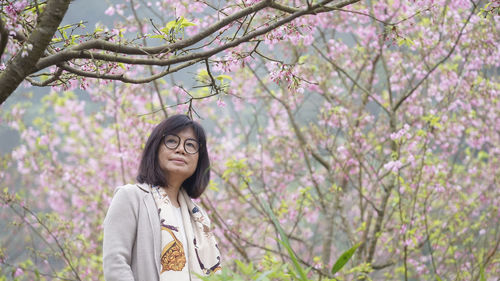 Portrait of smiling young woman standing by cherry tree