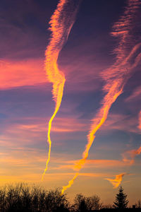 Low angle view of vapor trails in sky at sunset