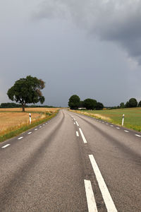 Empty road by trees against sky