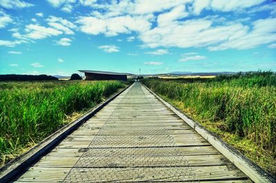 Road passing through field against cloudy sky