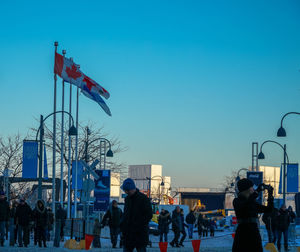 People by flags in city against clear blue sky