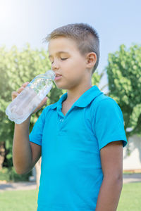 A young boy drinks water from a plastic bottle. vertical shot.