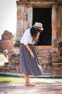Side view of mid adult woman wearing hat standing against old ruin