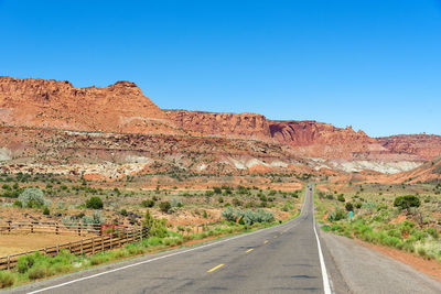 Road leading towards mountains against clear blue sky