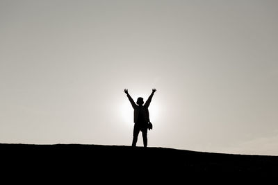 Silhouette woman with arms outstretched standing on hill against sky