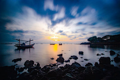 Silhouette rocks in sea against sky during sunset