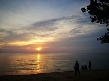 Silhouette people on beach against sky during sunset