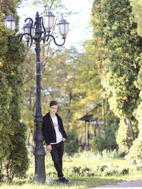 Young man looking away while standing by street light pole in park